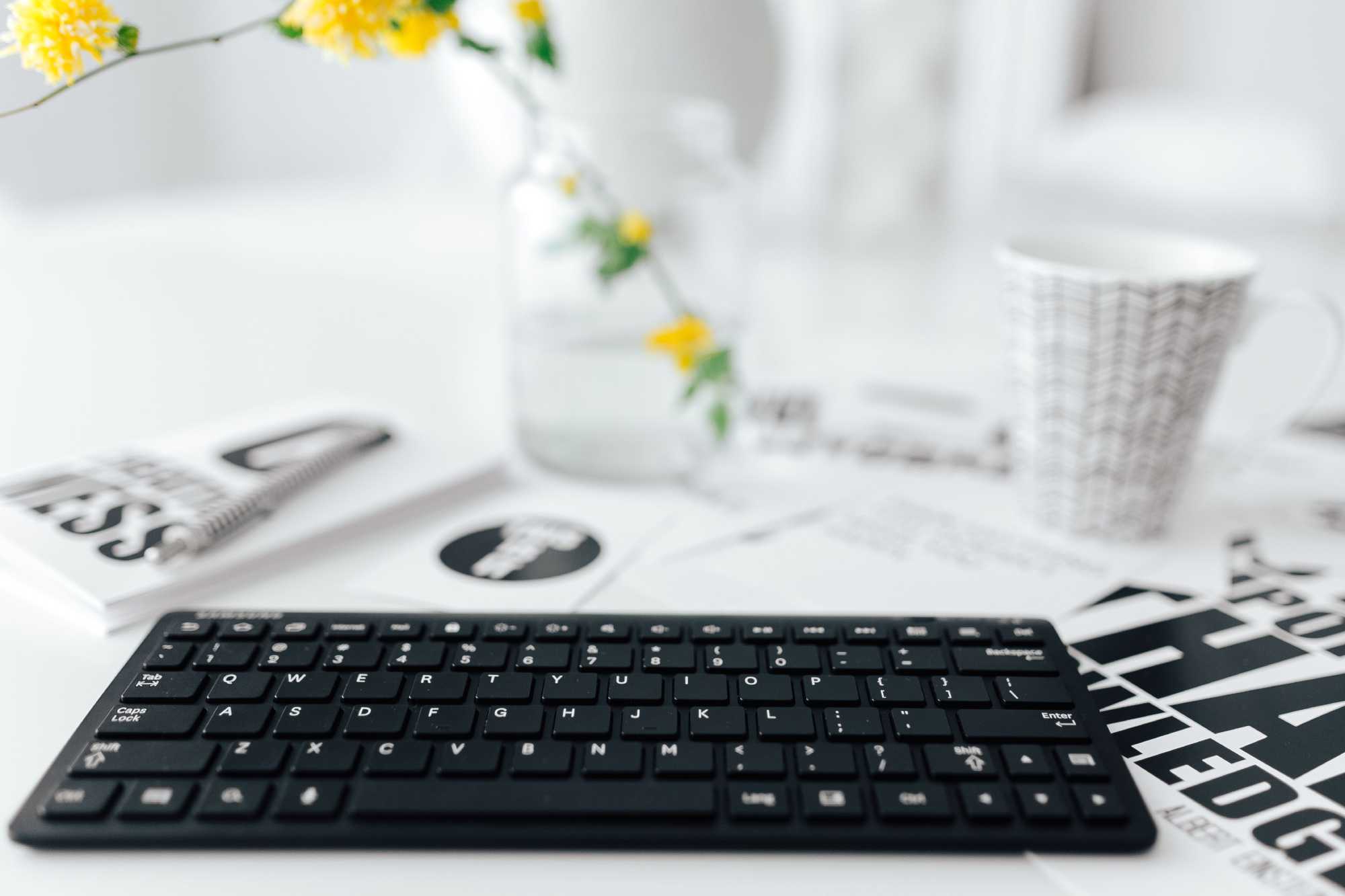 keyboard with notepad, flowers and coffee mug in the background