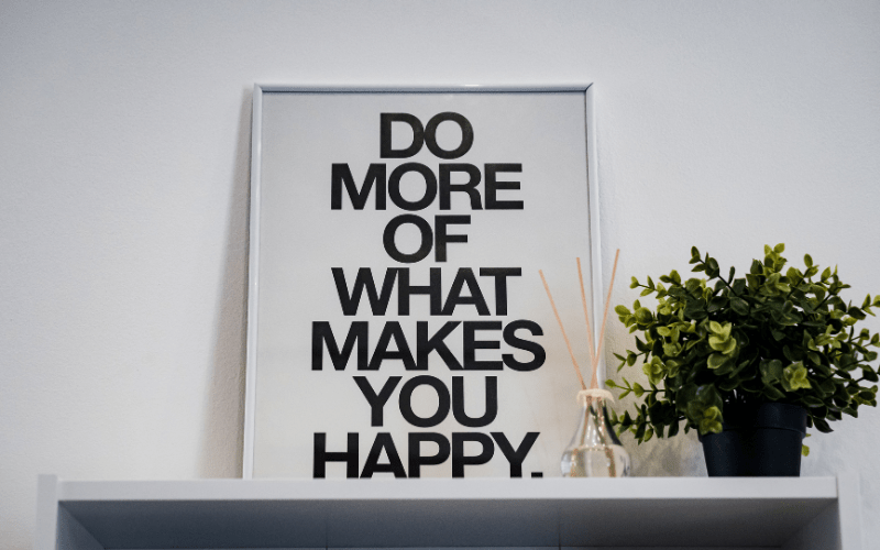 great parenting quotes: the words do more of what makes you happy on a white board with a frame. Next to the sing is an artificial plant in a black pot with fragrance next to it. The fragrance has sticks poking out of it and the sticks are in a clear jar