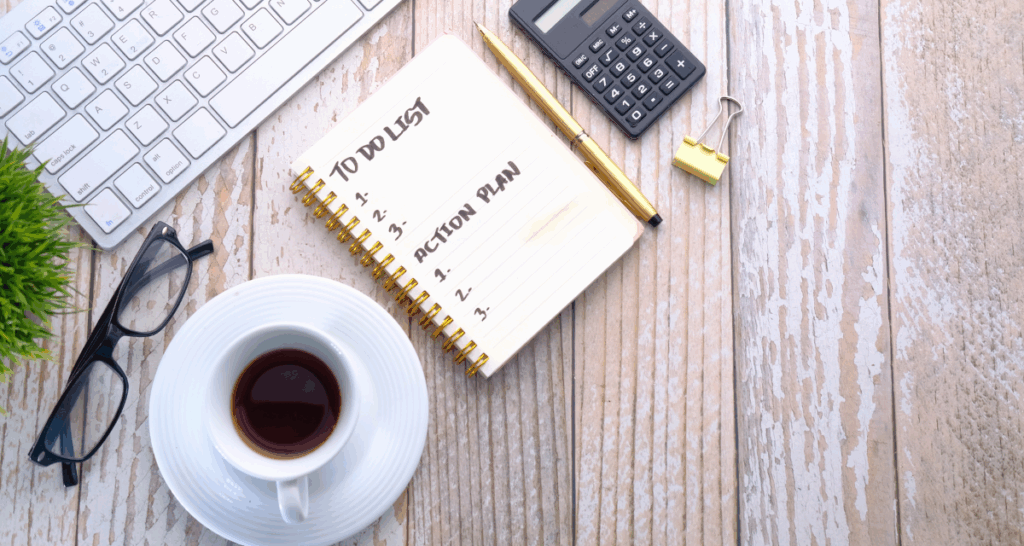 an image on a wooden background of a laptop, calculator, list, pen, glasses, tea cup, green shrub, clamp