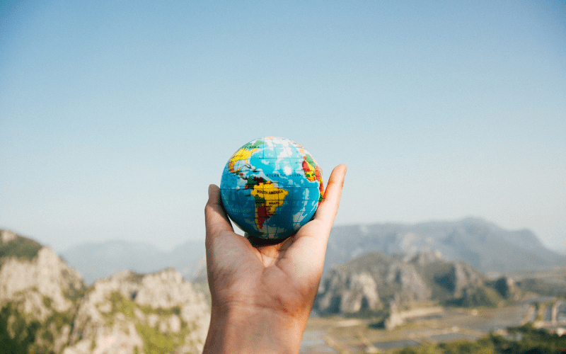 A hand holding the earth in the form of a small ball overlooking a beautiful canyon
