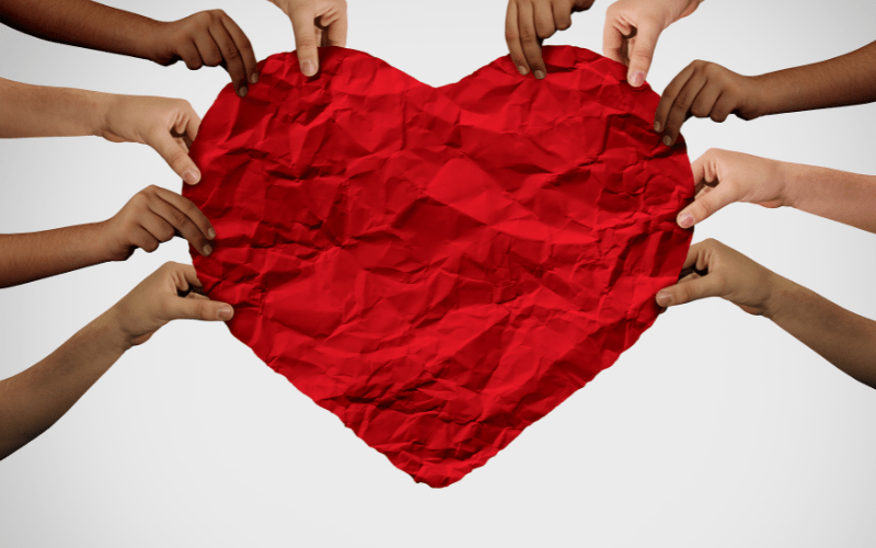 a giant red heart in a construction paper and little hands holding it up symbolizing helping others